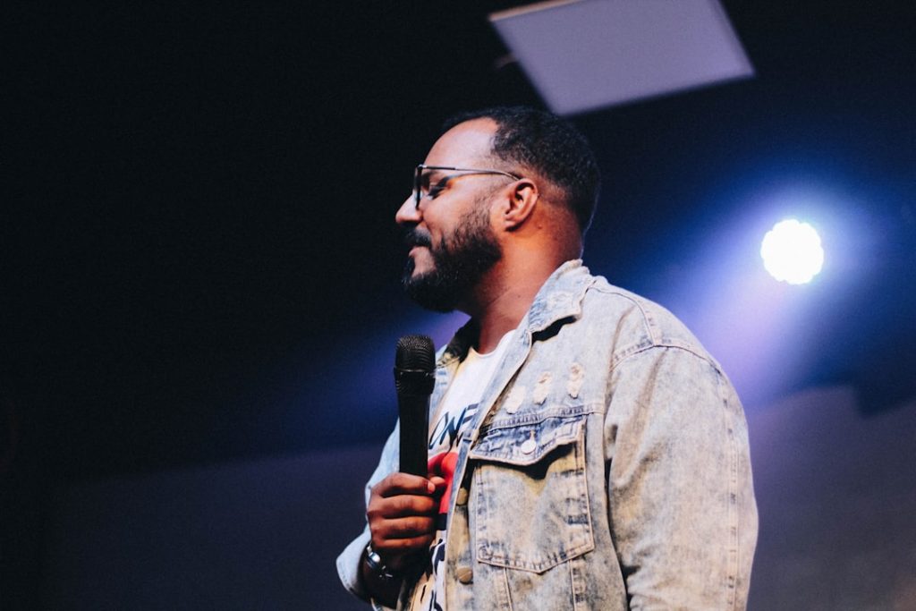 standing-man-wearing-blue-denim-button-up-jacket-while-holding-microphone-phb0ztr2cfe
